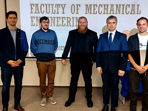 Eine Gruppe Männer steht vor einer Bildfläche mit der Aufschrift Faculty of Mechanical Engineering