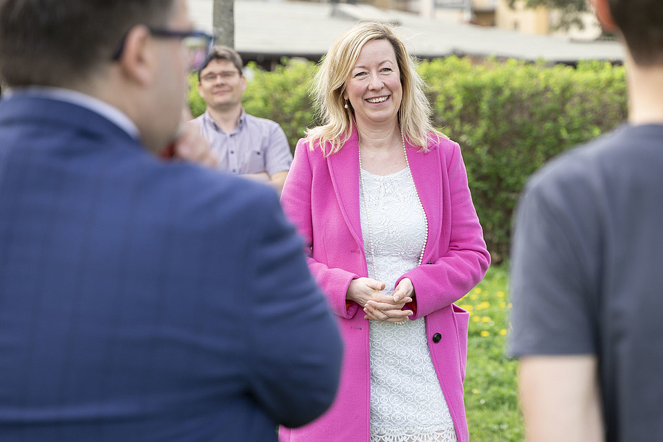 Prof. Dr. Sophia Keil in a bright pink jacket and white dress smiles during an outdoor conversation.