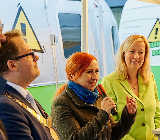 Franziska Schubert stands in front of the ZukLOS trailer and speaks into the microphone.