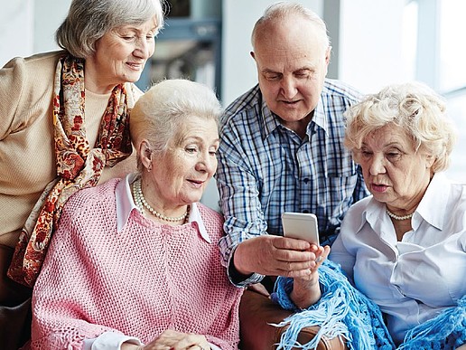 Vier Seniorinnen und ein Senior sitzen zusammen und schauen auf ein Handydisplay