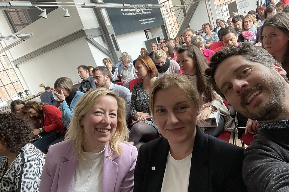 A selfie of Prof. Keil, Ms. Groß and Mr. Tiller, in the background the audience of the specialist consultants' conference.