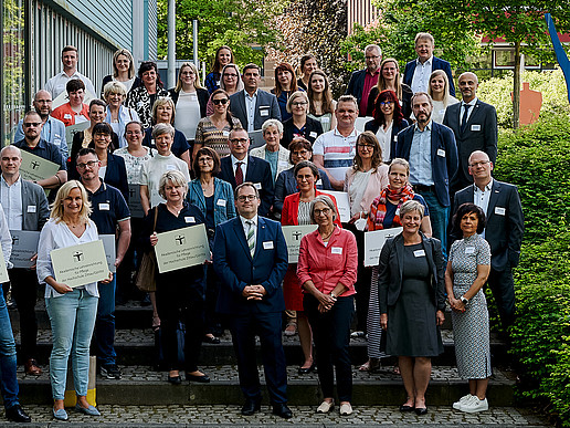 A group of university members and cooperation partners from the care sector stand next to the Blue Box on the Görlitz campus.