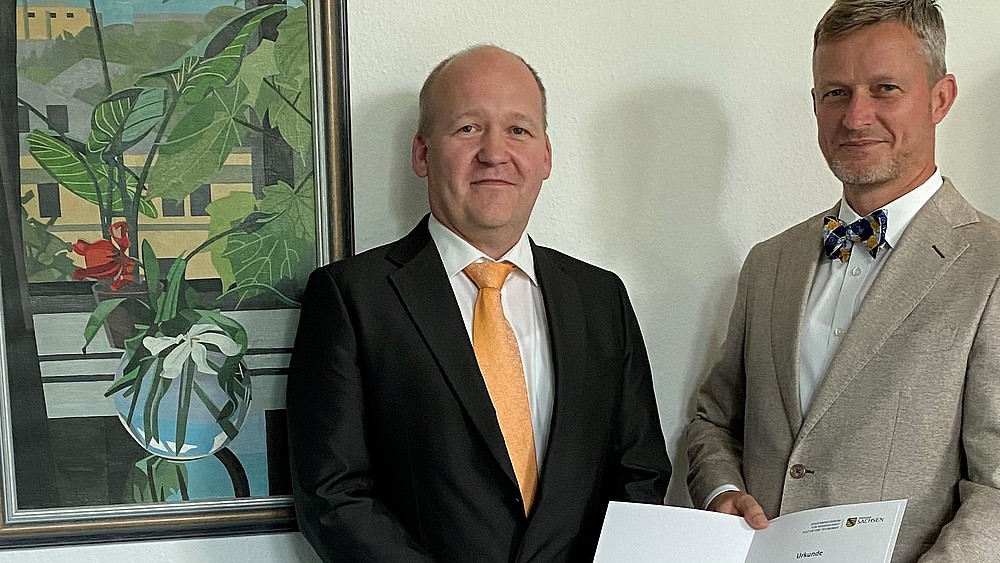 Christoph Matthias Duscha und Staatssekretär Handschuh bei der Übergabe der Ernennungsurkunde zum Kanzler an der HSZG in einem Raum im SMWK