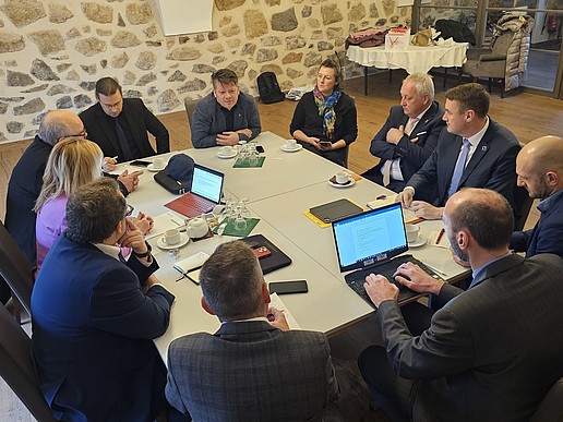 An einem Tisch sitzen viele Vertretende von Städten und Bildungseinrichtungen und unterhalten sich.