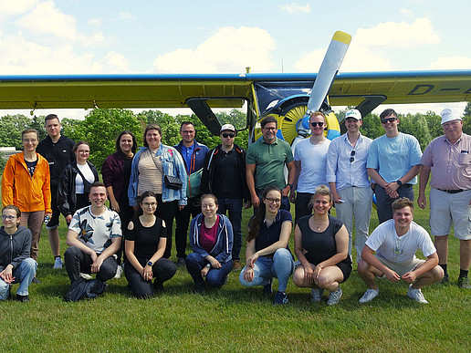 Gruppenbild: Studierende und Professoren stehen und hocken vor einem gelb-blauen Flugzeug.