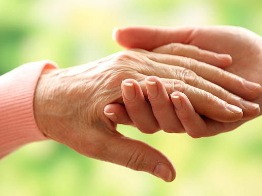 Two hands belonging to an old and a young woman hold each other.