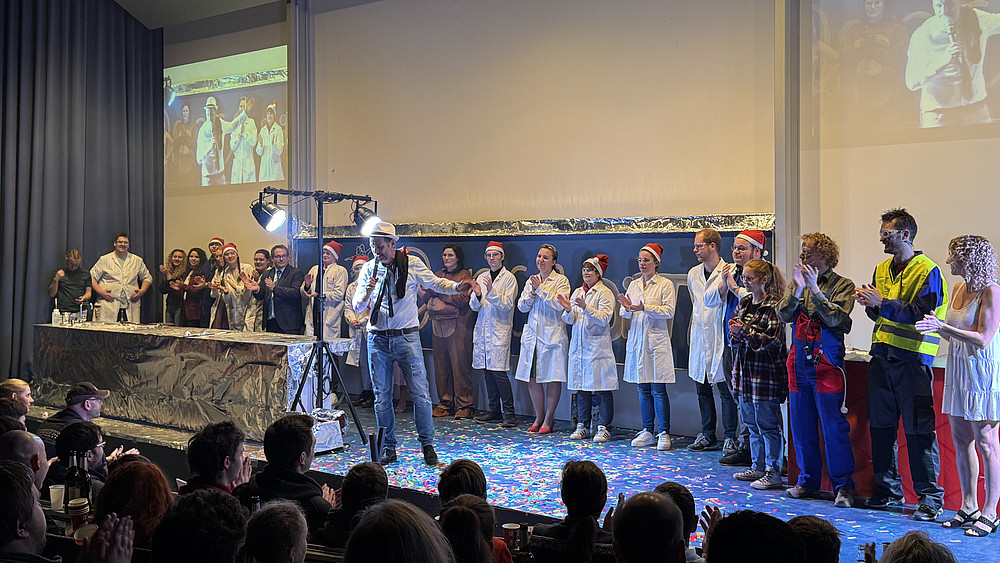 Das Schauvorlesungsteam steht in einer Reihe auf dem Vorlesungssaal-Podium und klatscht Beifall.