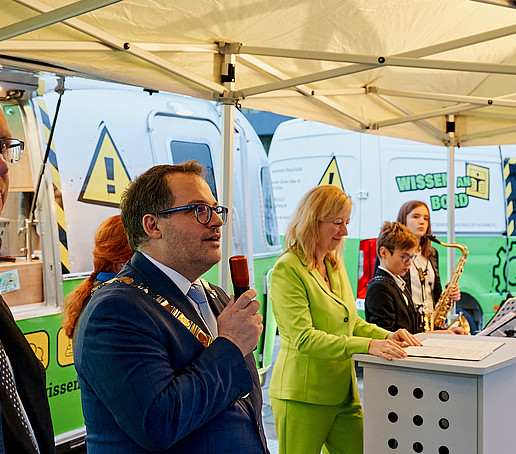 The Rector speaks into the microphone, next to him the Chairman of the University Council, the Vice-Rector and young brass players. They stand in front of the ZukLOS trailer.