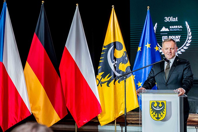 Ein Redner steht am Rednerpult, links von ihm sind die tschechische, deutsche und polnische Flagge zu sehen.