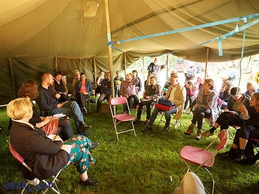 People sitting in a discussion circle under a tent