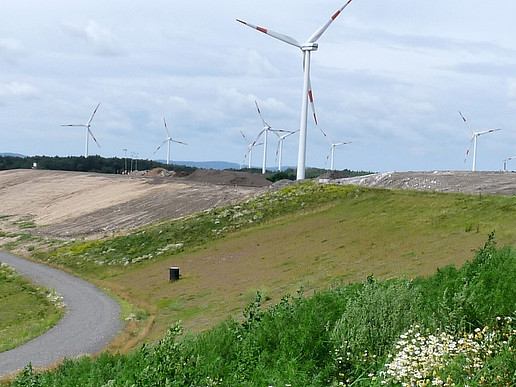 Waste management in practice. Exterior view of the Wetro landfill site. Green hills and cleared areas in the foreground, wind turbines in the background.