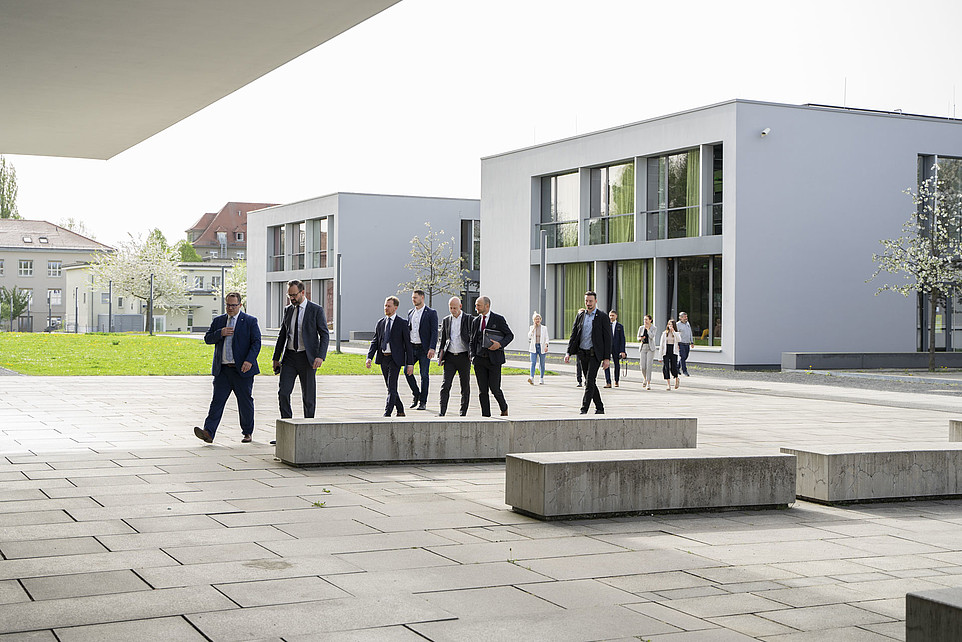 Group of formally dressed people walking through a modern campus.