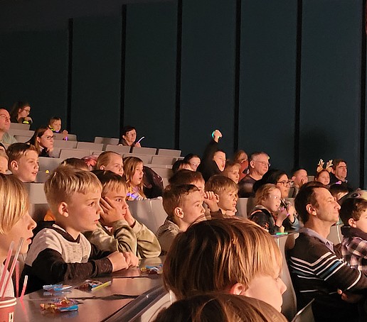 Children sit on rows of seats in the Audimax and look towards the stage.