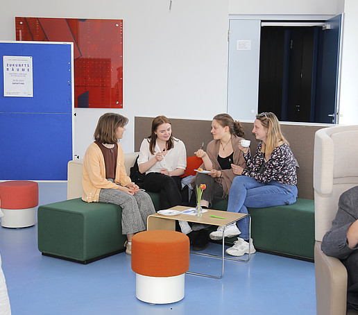 Studierende sitzen in Lounge-Möbeln und besprechen sich.