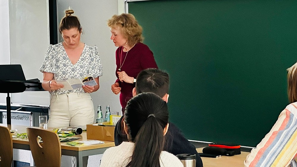 Kristin Groß and a Studienkolleg employee from Leipzig are standing in front of a blackboard in the seminar room looking at a flyer.