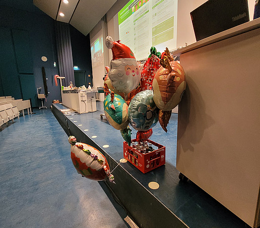 A crate of soda bottles with balloons tied to them stands on the stage in the Audimax.