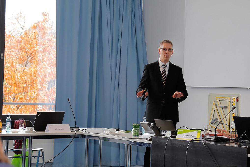 Male professor stands in front of a wall on which a presentation is projected and gives a lecture on the possibilities of new digital educational offers at the HSZG.