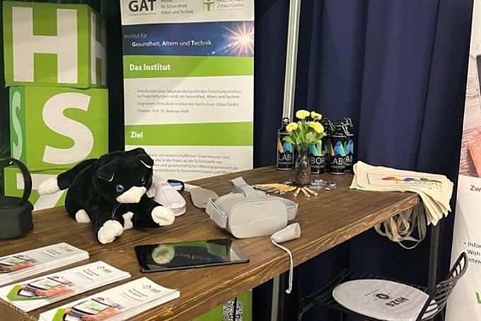 The GAT Institute's information stand with flyers on display and the fluffy cat as well as flowers and technical equipment.