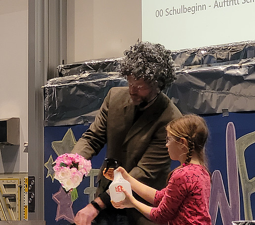 A girl and a man in a wig experiment on stage.