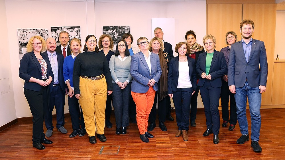 Representatives from the Alliance of Municipal Equal Opportunities Officers in Lusatia, among others, stand for a group photo in a room in front of a wall with black and white pictures and smile into the camera.