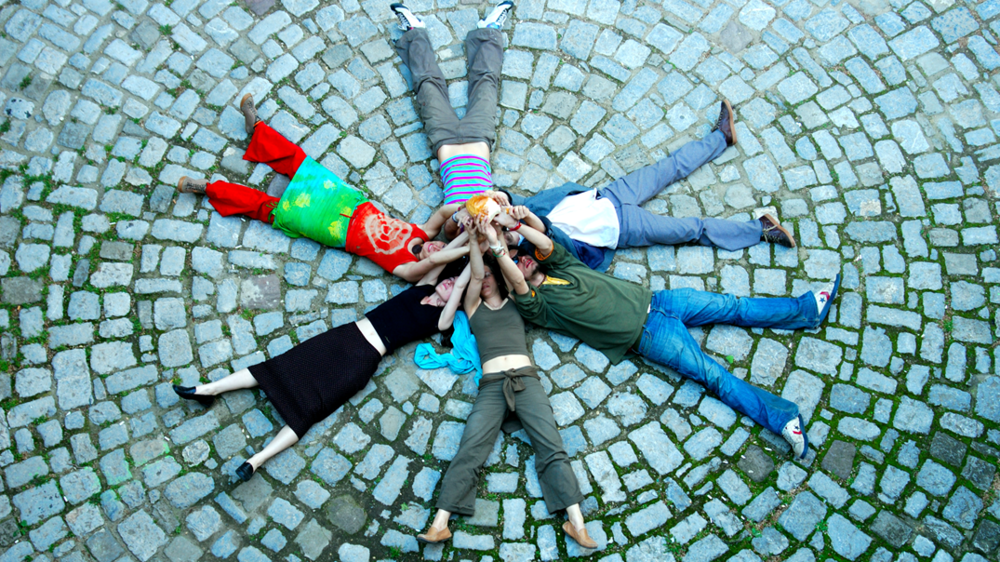 Students lie in a circle on a stone floor and stretch their arms towards a star.