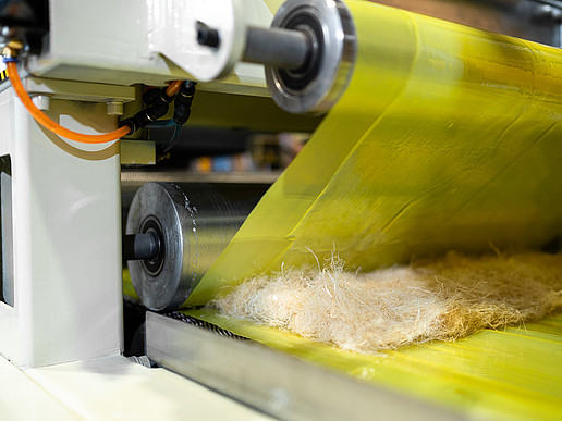 A roller picks up natural fibers and binds them into two yellow films.