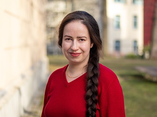 Anna Prenzel lächelt in die Kamera, sie steht auf einer Wiese neben einem Görlitzer Campusgebäude und trägt ein rotes Oberteil.