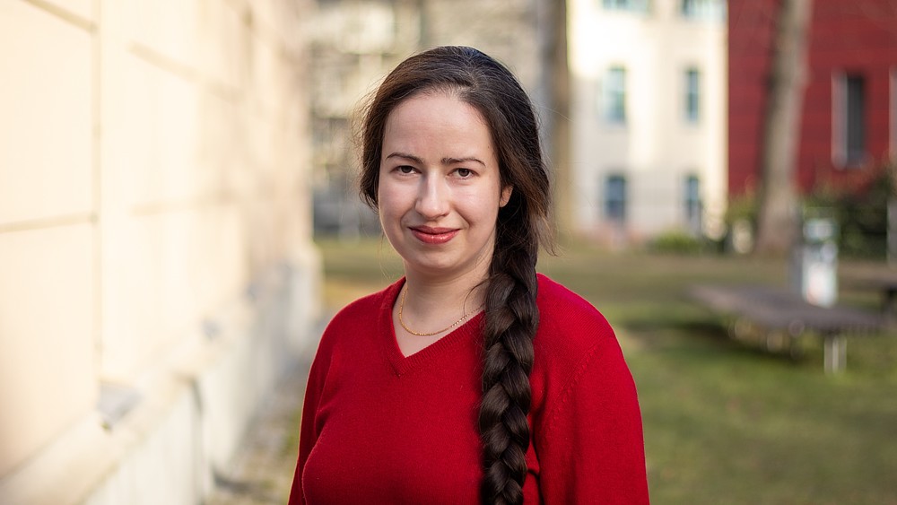 Anna Prenzel lächelt in die Kamera, sie steht auf einer Wiese neben einem Görlitzer Campusgebäude und trägt ein rotes Oberteil.