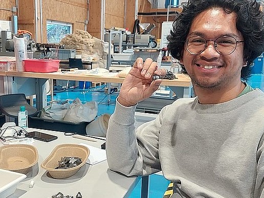 Faiz sits at his workstation in the Lander Technikum. In front of him are black plastic parts.