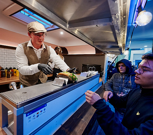 Ein Gast bekommt aus dem Speisewagen einen Hot-Dog gereicht.