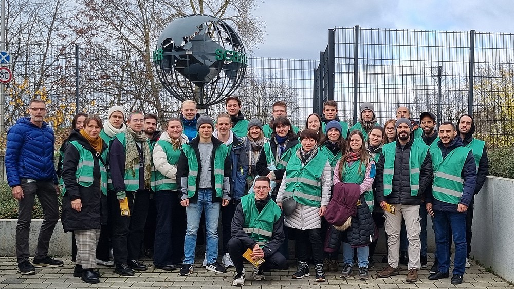 Eine Gruppe von Studierenden stehen als Gruppe nebeneinander, im Hintergrund steht ein Stahl-Globus.