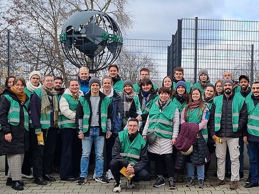 Eine Gruppe von Studierenden stehen als Gruppe nebeneinander, im Hintergrund steht ein Stahl-Globus.