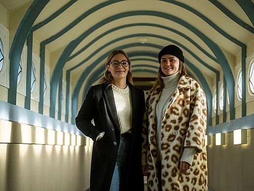Two female students stand in winter clothing in the university building in Görlitz.