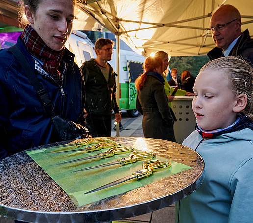 A student and a child look at five golden scissors lying on a high table.