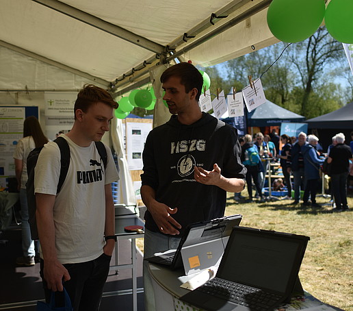 An employee explains an experiment to a visitor in the tent on a laptop.
