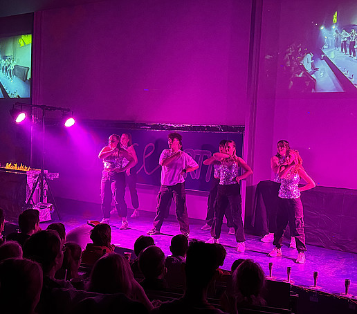 Eine Tanzgruppe tanzt auf dem Podium im lila Licht.