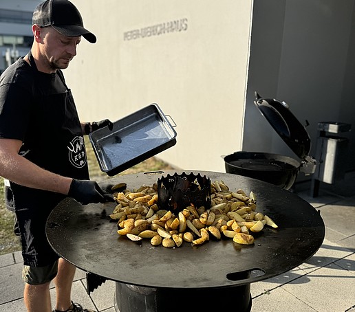 Ein Mann grillt Kartoffelecken auf einer Grilltonne.