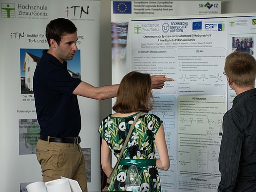 A researcher shows two visitors his research on the poster wall