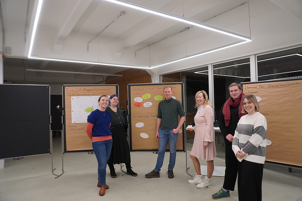 A group of workshop participants stand in front of wooden pinboards.