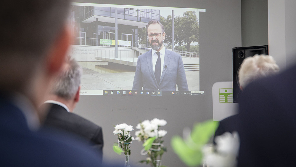 Video transmission via projector on a wall with Minister of State Gemkow. Guests watch his speech.