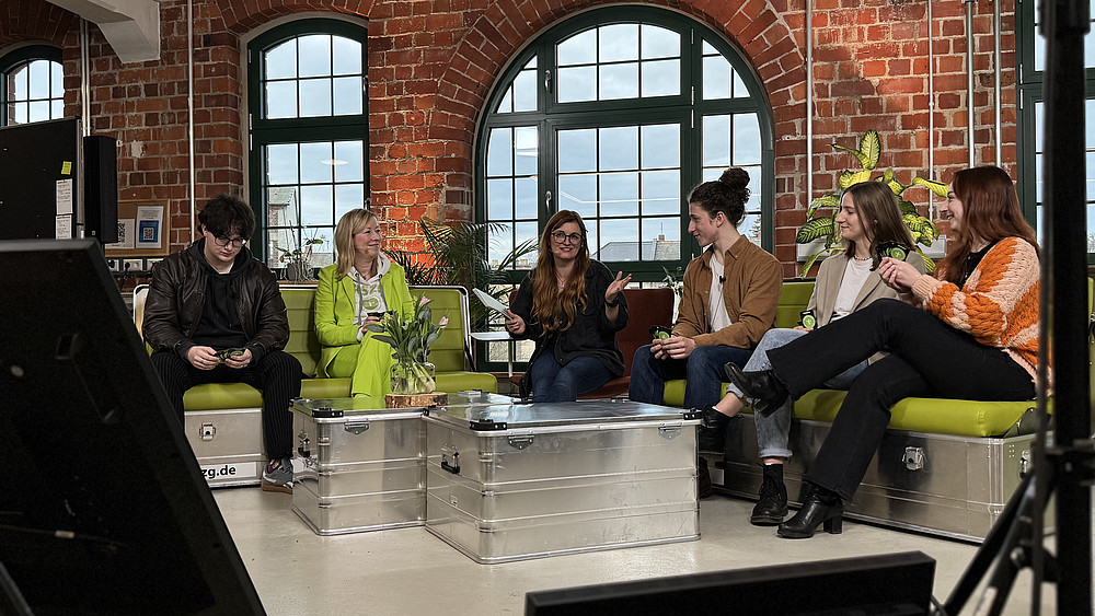 HIT participants sit on the green sofas in the studio and chat.