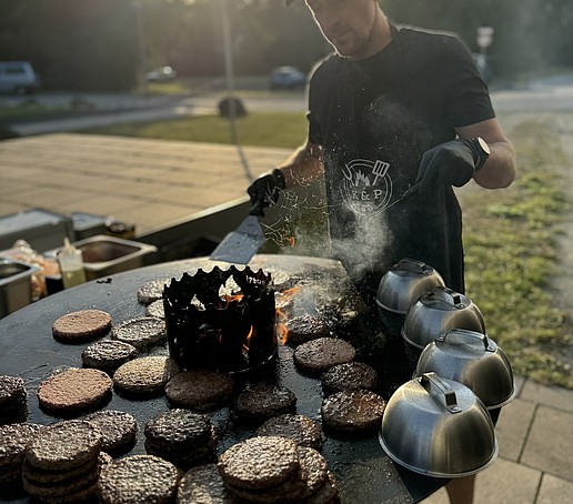 A man grills burgers on a barbecue barrel.