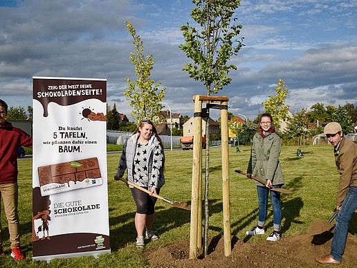 Four people plant a tree. Next to it is a roll-up with the advertising message.