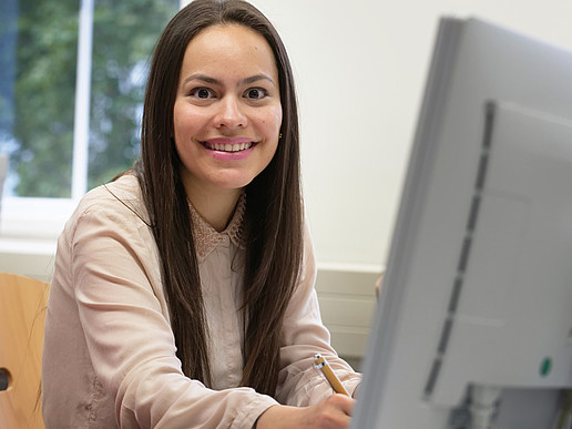 Smiling student sits in front of her PC and researches