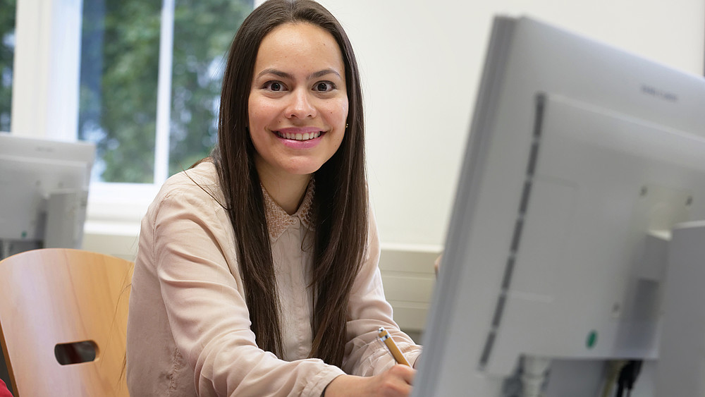 Smiling student sits in front of her PC and researches