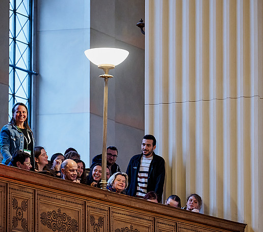 A student in the gallery stands and holds the microphone.