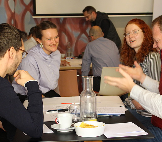 Participants sit at the table in conversation.