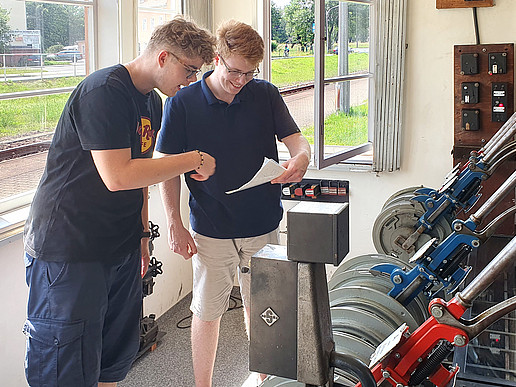 Im mechanischen Stellwerk auf dem Ausbildungsbahnhof Zittau Süd stellen zwei Schüler die Fahrstraße ins Gebirge mit viel Muskelkraft ein und schauen sich dazu Pläne an.