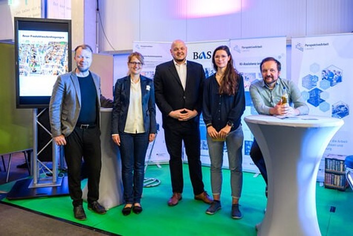 Employees of the PAL team stand in front of roll-ups and look into the camera.