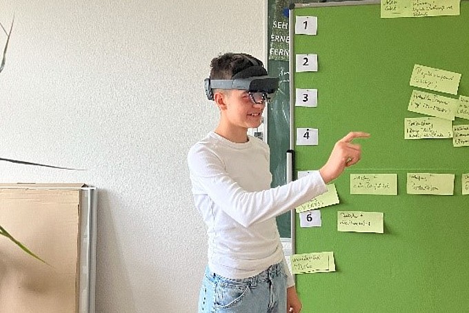 Student wears augmented reality glasses and raises his right arm.